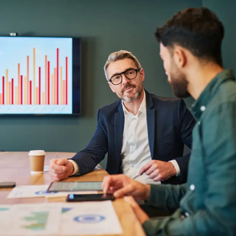 Two men in business attire discussing financial charts in a meeting room